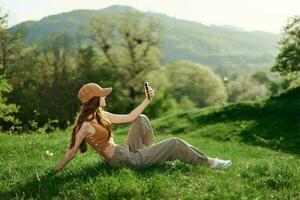 blogueur avec téléphone travail dans parc sur herbe par arbre, pigiste mode de vie photo