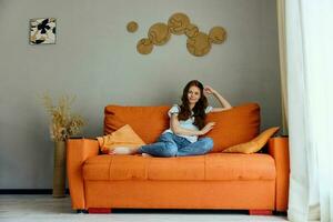 jolie femme sur le Orange canapé dans le du repos pièce posant inchangé photo