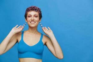 Jeune athlétique mode femme avec coloré cheveux et court la Coupe de cheveux posant et dansant dans bleu tenue de sport souriant et à la recherche à le caméra fermer sur une bleu monochrome Contexte photo