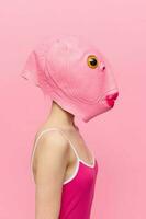 marrant fou femme sur une rose Contexte permanent dans une poisson tête masque sur une rose arrière-plan, conceptuel Halloween costume art photo