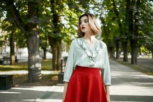 jolie blond dans rouge jupe en plein air dans le parc vert des arbres photo