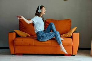 femme sur le Orange canapé écoute à la musique avec écouteurs mode de vie photo