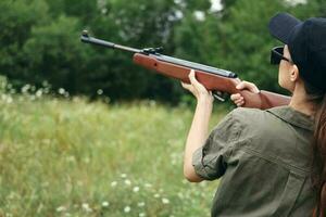 femme sur Extérieur en portant une pistolet près le sien tête vue chasse vert feuilles photo