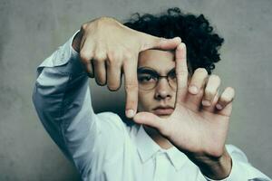 à la mode gars avec frisé cheveux faire des gestes avec le sien mains sur une gris Contexte portrait fermer photo