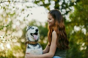 une femme avec une rauque race chien sourit et affectueusement coups sa bien-aimée chien tandis que en marchant dans la nature dans le parc dans l'automne contre le toile de fond de le coucher du soleil photo