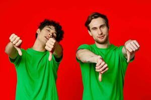 deux copains dans vert t-shirts sont permanent côté par côté posant relation amicale rouge Contexte photo