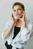 Jeune femme adolescent écoute à la musique avec infertile écouteurs et dansant maison, sourire avec les dents avec une court la Coupe de cheveux dans une blanc chemise sur une blanc Contexte. fille Naturel pose avec non filtres photo