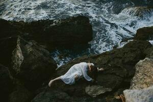 pieds nus femme dans une isolé place sur une sauvage rocheux côte dans une blanc robe vue de au dessus photo