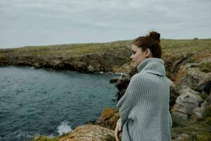 portrait de une femme dans une gris chandail des stands sur une rocheux rive la nature mode de vie photo