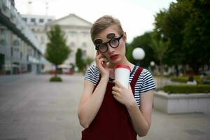 une femme avec des lunettes des promenades autour le ville une verre avec une boisson loisir la communication photo