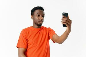 Beau homme de africain apparence en portant une mobile téléphone dans de face de le sien visage sur une lumière Contexte photo