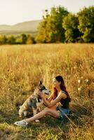 femme séance dans champ avec teckel chien souriant tandis que dépenses temps dans la nature avec ami chien dans l'automne à le coucher du soleil tandis que en voyageant photo
