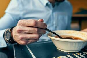 une homme mange Bortsch avec acide crème dans une restaurant à une table dans une café et une regarder sur le sien main photo