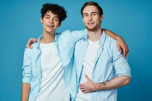 Jeune Hommes dans bleu chemises étreindre sur isolé Contexte copains amusement photo