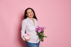 souriant Enceinte femme, exprimer bonheur attendant pour bébé, posant avec bouquet de tulipes et cœur en forme de cadeau boîte photo