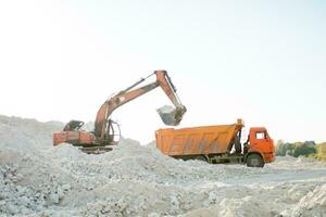 le excavatrice recueille des pierres dans une seau et met leur dans une camion. travail Machines à route construction photo