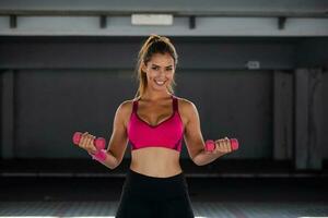 femme en forme forte travaillant avec des haltères. une femme en forme attrayante s'entraîne avec des haltères comme concept de remise en forme. femme active en vêtements de sport travaillant. photo