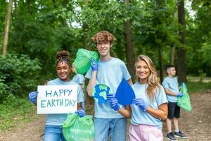 diverse groupe de gens cueillette en haut poubelle dans le parc bénévole communauté service. content international bénévoles en portant placard avec 'content Terre jour' message. photo