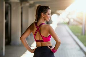 Jeune sportif femme entraînement. femme Faire faire des exercices des exercices sur rue. magnifique athlétique en forme fille dans brillant des sports Vêtements élongation sa bras et relaxant après aptitude formation sur rue. photo