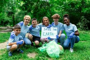 diverse groupe de gens cueillette en haut poubelle dans le parc bénévole communauté service. content international bénévoles en portant placard avec 'sauvegarder le Terre' message. photo