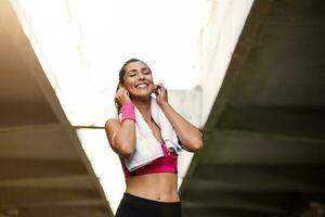 Jeune magnifique femme jogging, aptitude tenue, écoute à la musique sur écouteurs, téléphone intelligent, mer lever du soleil, maigre parfait svelte corps, en bonne santé vivant mode de vie, été, souriant, content photo