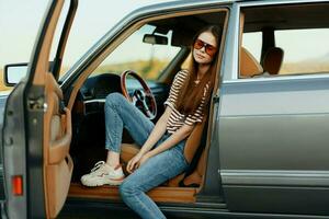 une femme chauffeur dans des lunettes de soleil arrêté le voiture sur le route dans une pktkshestvie et est repos à la recherche à une magnifique vue photo