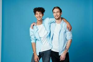 gars avec frisé cheveux dans une chemise et une T-shirt sur une bleu Contexte et une Jeune homme copains amusement photo