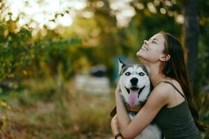 une femme avec une rauque race chien sourit et affectueusement coups sa bien-aimée chien tandis que en marchant dans la nature dans le parc dans l'automne contre le toile de fond de le coucher du soleil photo