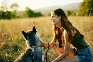 femme en marchant sa rauque chien et souriant Heureusement avec les dents sur une la nature marcher sur le herbe dans le l'automne coucher de soleil, mode de vie chien ami photo