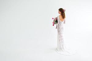 mariée fille joyeuse dans une robe tricotée blanche posant avec un bouquet de fleurs photo