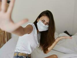 femme dans un isolé pièce sur le lit avec une médical masque faire des gestes avec sa mains photo