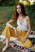 Jeune magnifique hippie femme séance sur le sol dans la nature dans le l'automne dans éco Vêtements dans le le coucher du soleil lumière, une mode de vie de Voyage et harmonie avec le monde photo