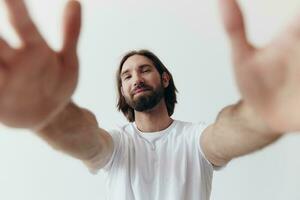 content adulte homme avec une barbe sourit et tire le cuisinier dans le caméra écoute à la musique dans écouteurs dans une affligé T-shirt sur une blanc isolé Contexte photo