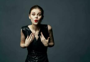 une femme dans une noir robe gestes avec sa mains surprise délice émotions. photo