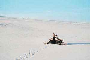 jeune couple, un mec et une fille avec des émotions joyeuses dans des vêtements noirs marchent à travers le désert blanc