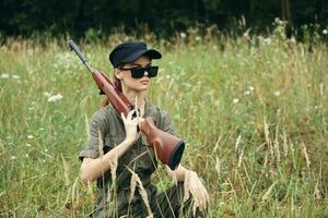 femme sur la nature est assis dans une abri avec une arme foncé des lunettes noir casquette vert photo