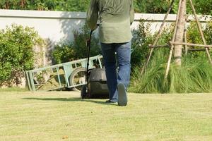 Retour portrait de jardinier poussant la tondeuse à gazon sur le terrain en herbe photo