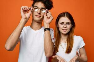 frisé gars et une fille dans blanc t-shirts sont permanent suivant à chaque autre sur un Orange Contexte photo