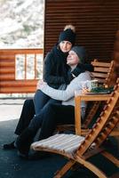 Couple de jeunes un gars et une fille sur le porche d'une maison en bois couverte de neige photo