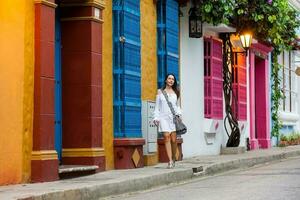 magnifique femme sur blanc robe en marchant seul à le coloré des rues de le colonial fortifiée ville de Carthagène de Indes photo