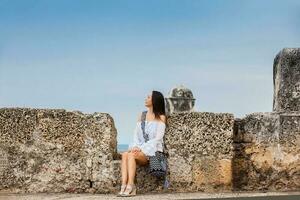 magnifique femme sur blanc robe séance seul à le des murs alentours le colonial ville de Carthagène de Indes photo