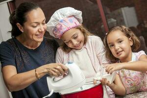 mère et filles ayant amusement dans le cuisine cuisson ensemble. en train de préparer petits gâteaux avec maman photo