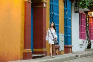 magnifique femme sur blanc robe en marchant seul à le coloré des rues de le colonial fortifiée ville de Carthagène de Indes photo