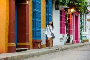 magnifique femme sur blanc robe en marchant seul à le coloré des rues de le colonial fortifiée ville de Carthagène de Indes photo