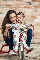 magnifique Jeune mère en jouant avec sa un année vieux bébé en plein air. avec maman équitation mon tricycle photo