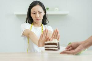 régime, suivre un régime mauvais pour la santé asiatique Jeune femme main dans pousser dehors, rejetant manger Chocolat gâteau ou sucré goût, combat à garder il de avoir graisse lorsque la personne apporter à moi. en bonne santé, nutrition de poids perte photo