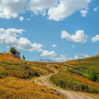 enroulement chemin par montagnes. trekking Montagne piste. brillant panoramique alpin paysage avec saleté route parmi herbes dans hauts plateaux. sentier montée. façon en haut flanc de montagne. photo