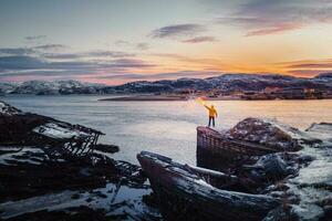 une Jaune figure avec une lumière du feu. cimetière de navires, hiver le coucher du soleil vue dans un vieux pêche village sur le rive de le barents mer, le kola péninsule, teriberka photo