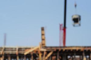 Photo défocalisée de la grue transportant le godet en métal de ciment mixte sur le chantier de construction avec fond de ciel bleu. l'image est floue exprès