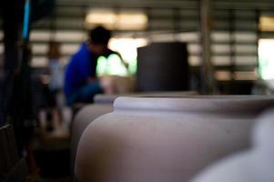 Photo gros plan de la poterie d'argile traditionnelle dans l'usine avec travailleur flou travaillant en arrière-plan